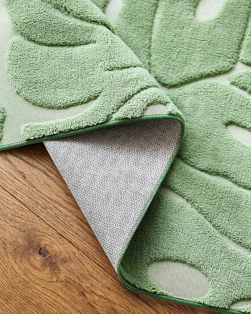 Close-up of sage green Monstera washable area rug with raised leaf texture and non-slip backing