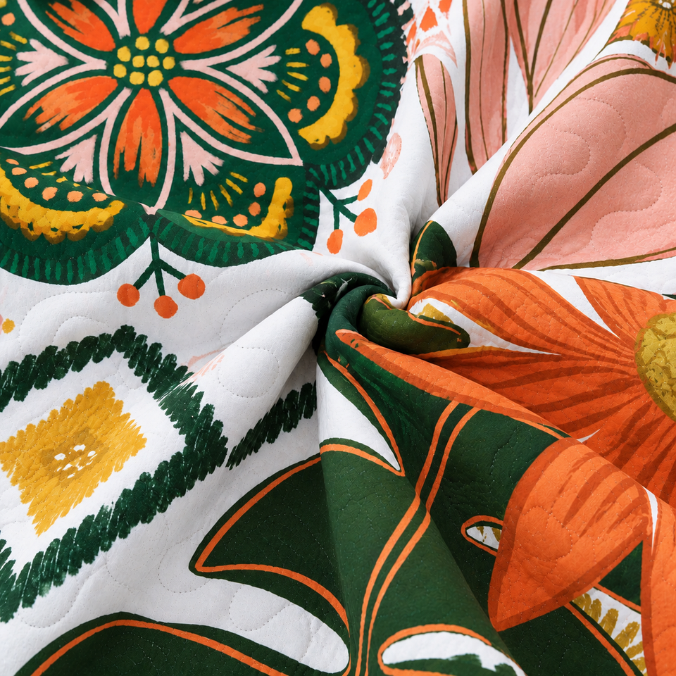 Gathered folds of the Flore quilt in Blush Pearl, with orange flowers and dark green leaves on white fabric.