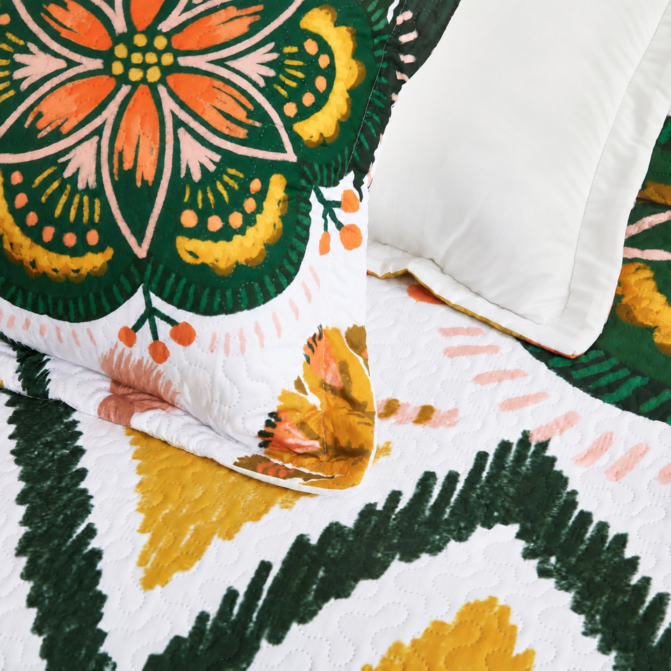 Flore quilt and sham in Blush Pearl, showing green, orange and yellow floral motifs and quilting on white fabric.