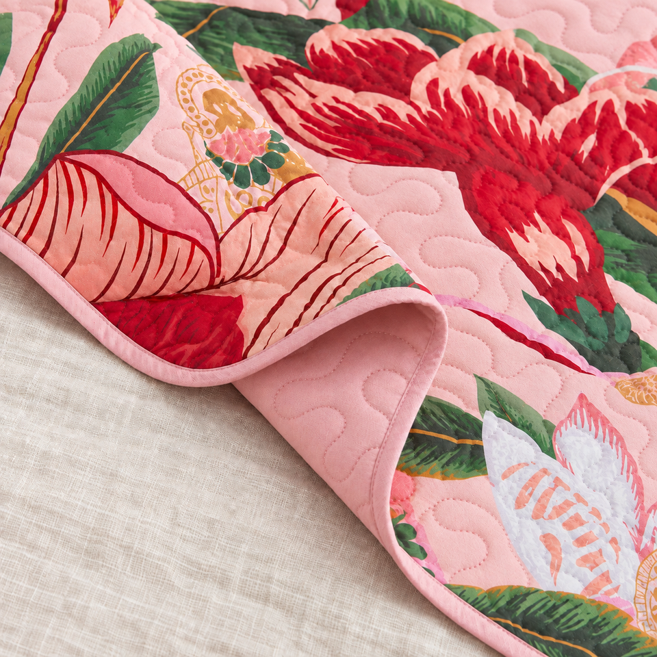 Flore quilt in Boho Rose folded to show its pink reverse, bound edge and red floral front.