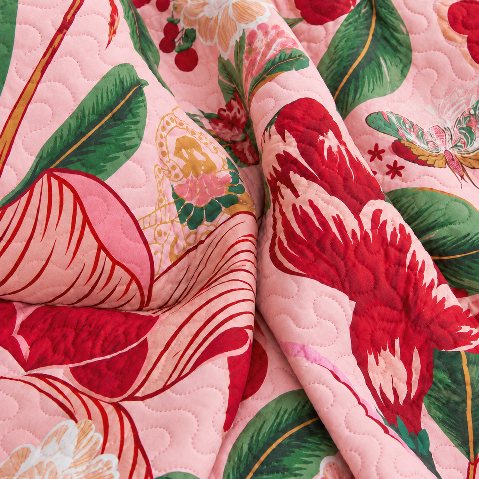 Gathered folds of the Flore quilt in Boho Rose, with red flowers and green leaves on a pink background.