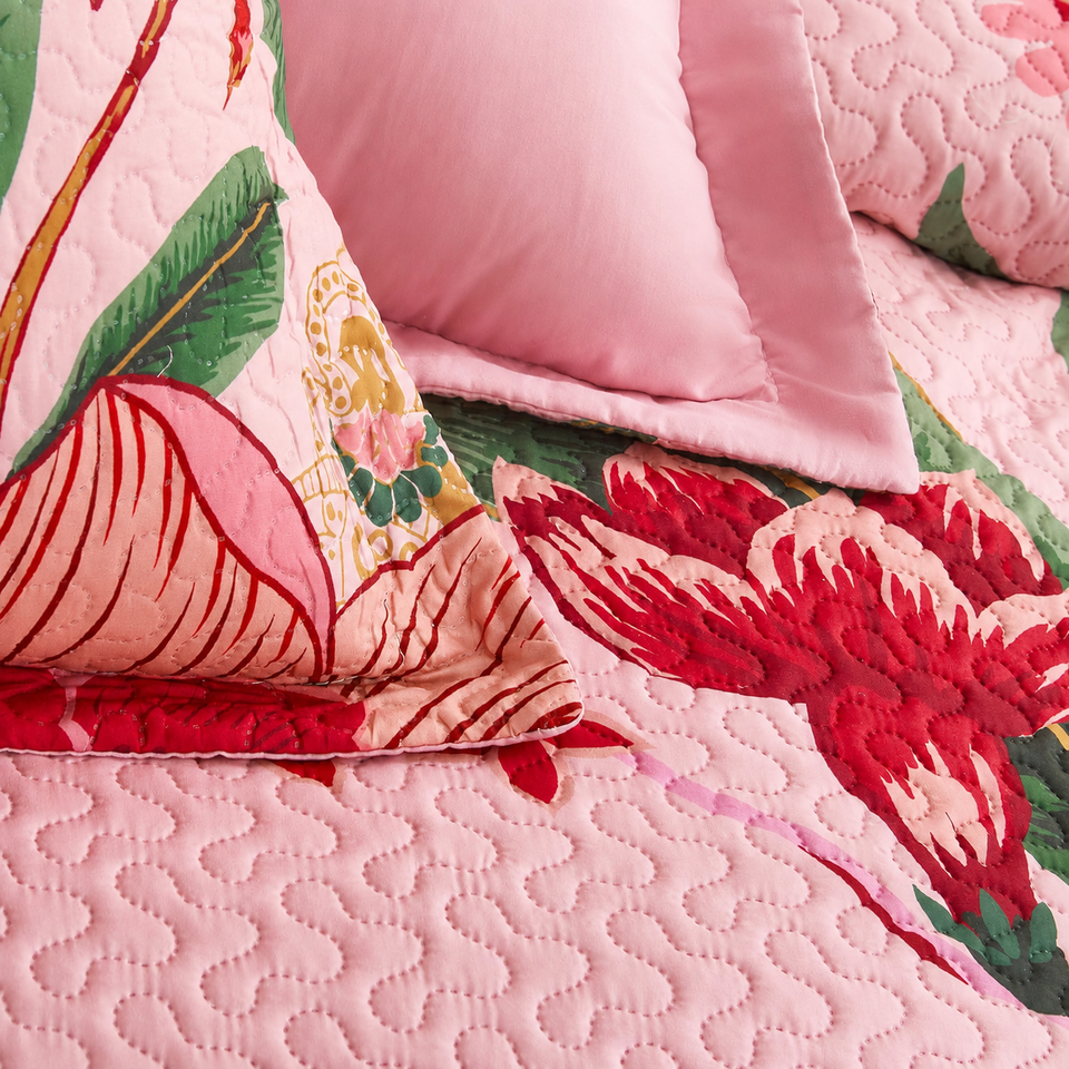Flore quilt and sham in Boho Rose, showing red flowers, green leaves and curved quilting on pink fabric.