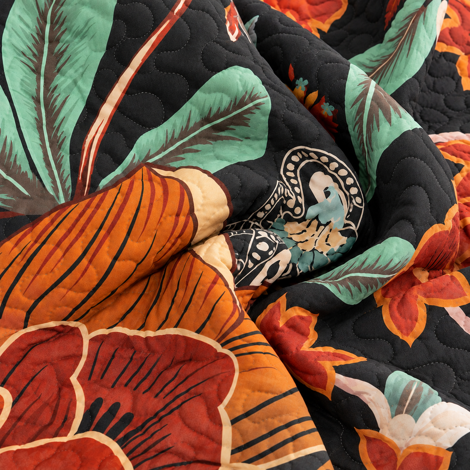 Gathered folds of the Flore quilt in Mocha Noir, with orange flowers and mint-green leaves on a black background.