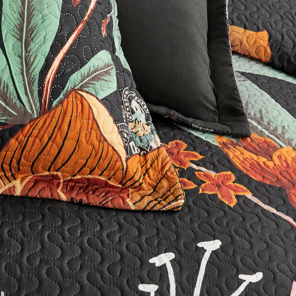 Flore quilt and sham in Mocha Noir, showing orange flowers, mint-green leaves and curved quilting on black fabric.