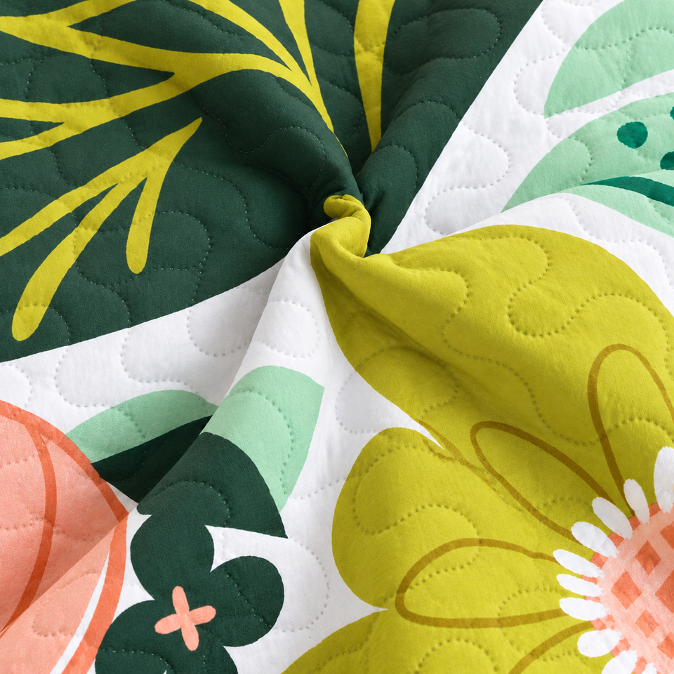 Gathered folds of the Flore quilt in Rose Garden, with yellow-green flowers and dark green leaves on white fabric.