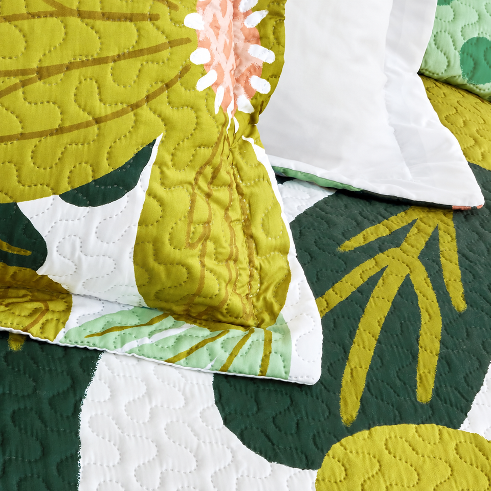 Flore quilt and sham in Rose Garden, showing yellow-green flowers, dark green leaves and quilting on white fabric.