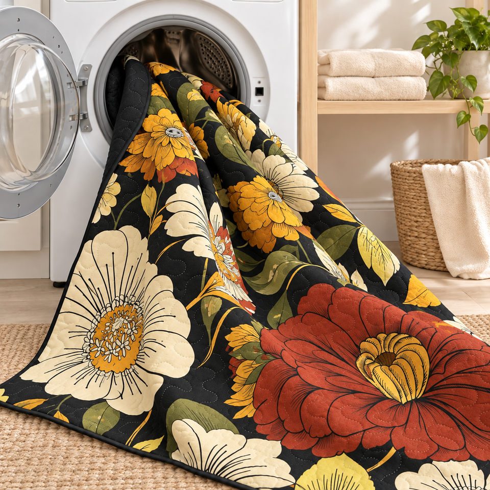 Flore quilt in Warm Ember draped from an open front-loading washer, showing cream and gold flowers on black fabric.